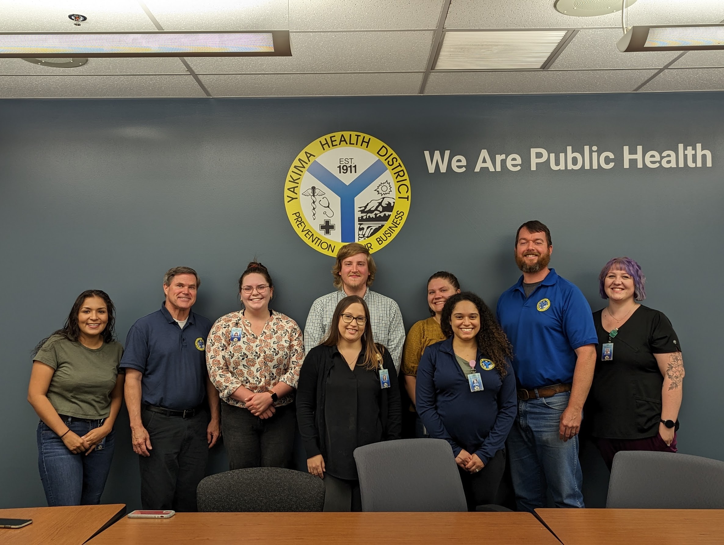 Picture of PROTEC17 Yakima Health members standing in front of their logo on a wall.