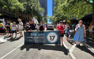 Image of PROTEC17 Executive Director Karen and others holding the PROTEC17 banner at the Pride parade.