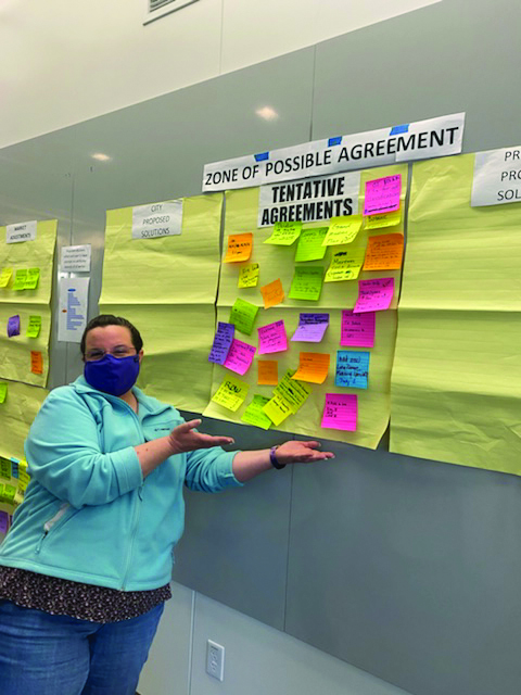 Image of PROTEC17 bargaining team member Janet Strahl pointing to the final tentative agreements (post-its and large note paper on the wall).