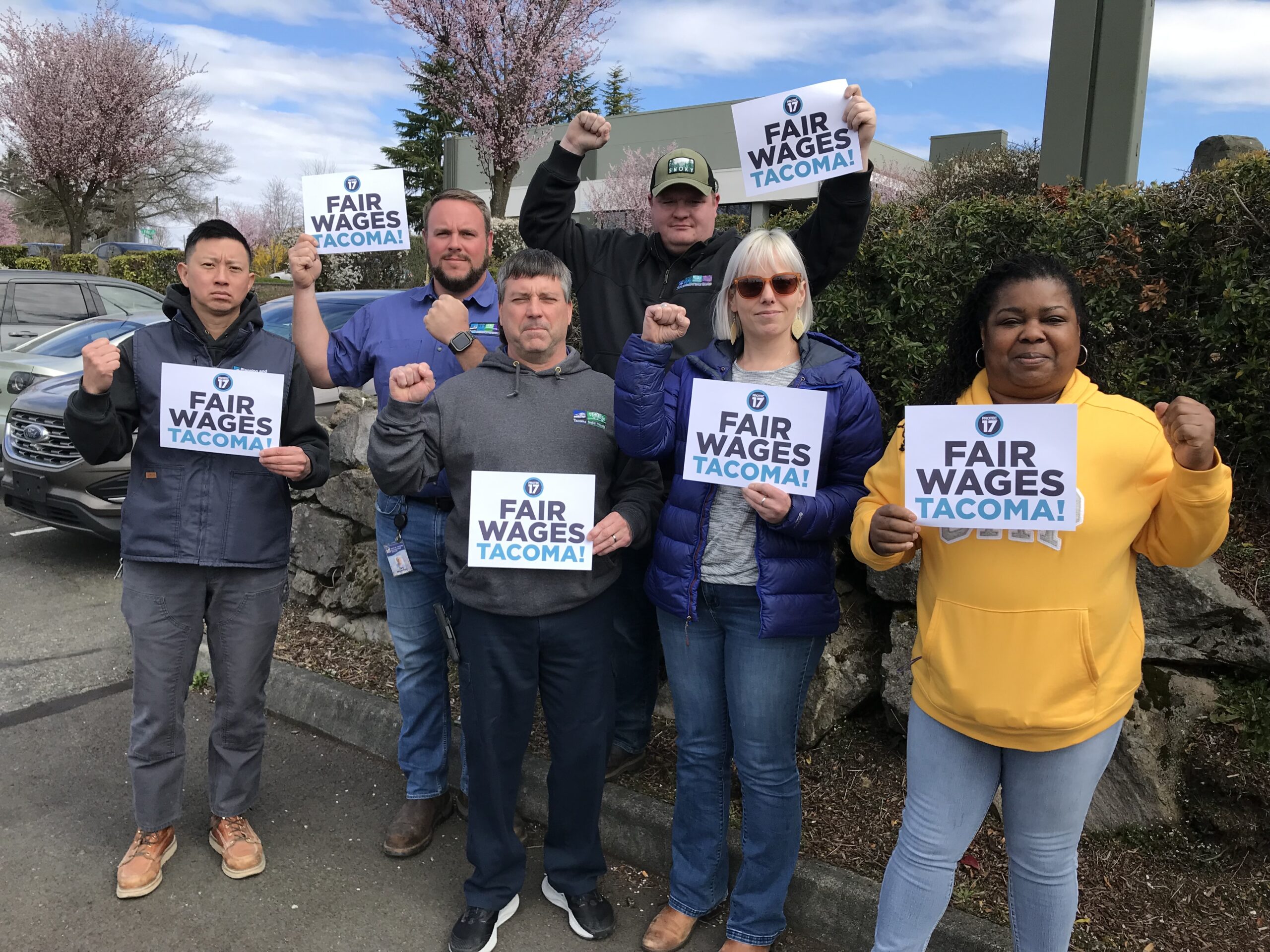 Picture of the City of Tacoma bargaining team posing with their fists raised in solidarity and holding signs that read, "FAIR WAGES TACOMA!"