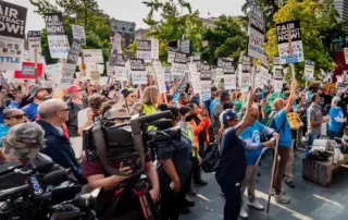 A huge crowd of Coalition of City Unions members gather outside Seattle City Hall. Folks are wearing their union gear/swag and holding up their "FAIR CONTRACT NOW!" signs and raising their fists in solidarity.