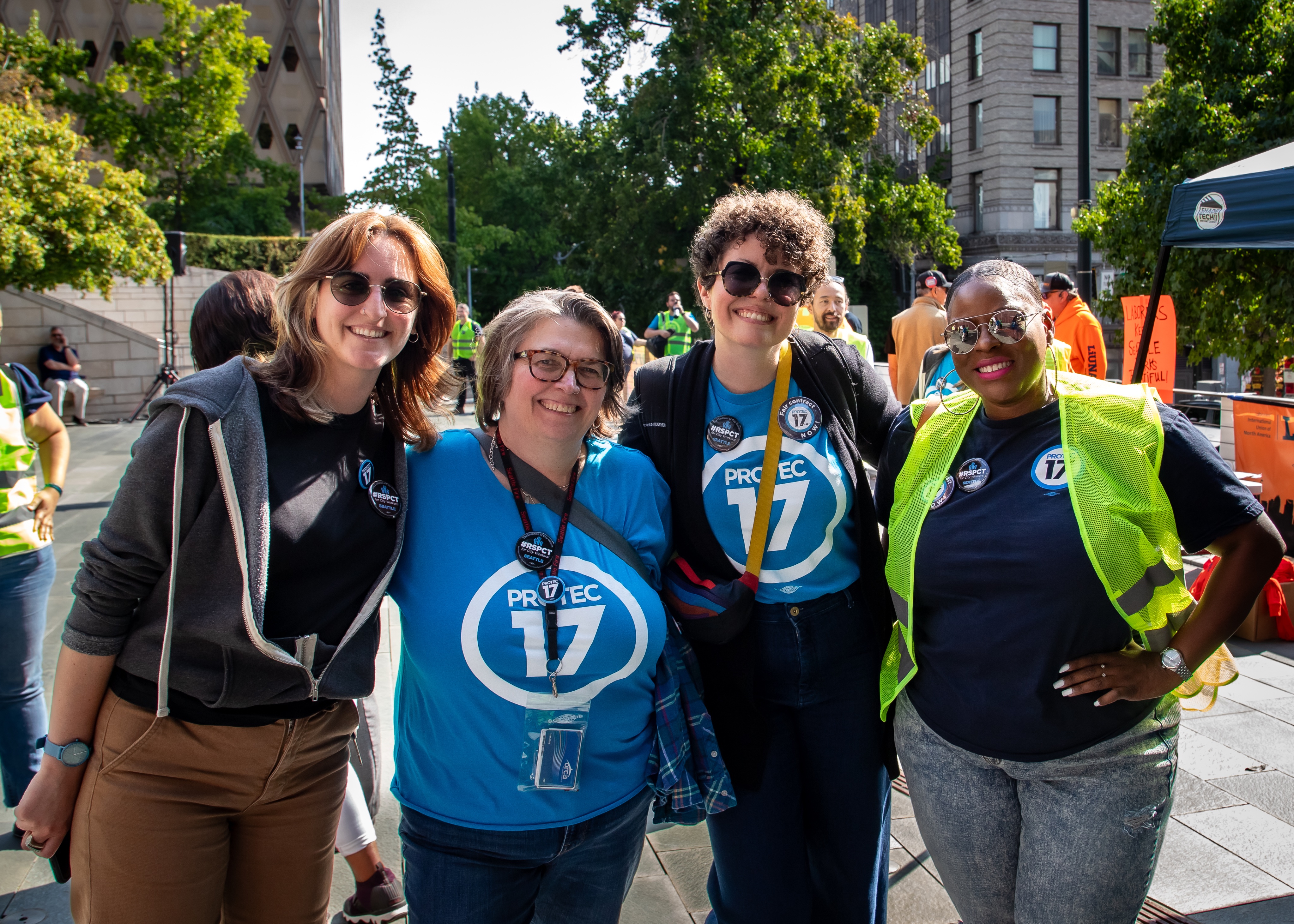 PROTEC17 members and staff smiling outside City Hall in the sun. They are wearing PROTEC17 shirts and buttons.