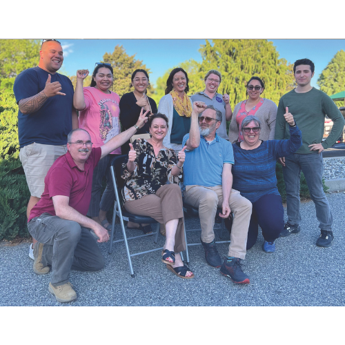 The Chelan-Douglas Health District (CDHD) bargaining team from 2023 stands together on a paved walkway with a beautiful green tree in the background. Everyone is smiling and showing positive hand gestures like thumbs ups.