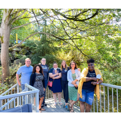 The Executive Board poses for a picture at their 2022 retreat. They are standing on an outdoor deck/staircase at a park, with beautiful green foliage in the background.