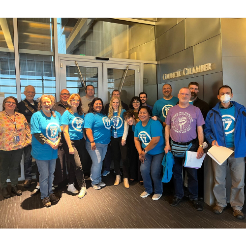 Seattle Members post with Lawmakers at Seattle City Hall. They are wearing their bright turquoise PROTEC17 shirts and beaming with bright smiles.