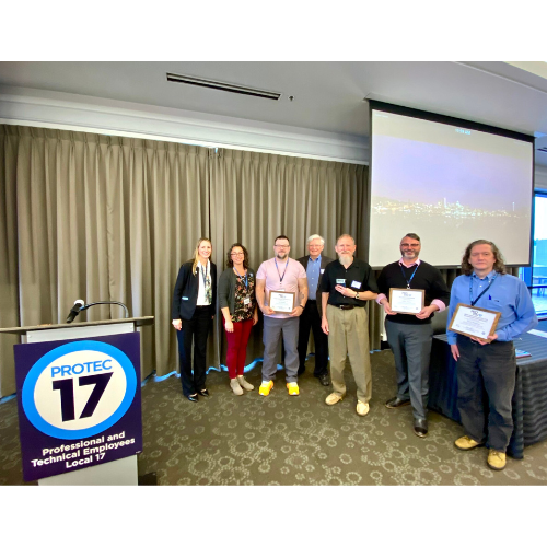 All of the REC member leaders who won awards are standing together with PROTEC17 President Rachel Brooks and Executive Director Karen Estevenin. The PROTEC17 podium is pictured to the left that reads, "Professional and Technical Employees Local 17."